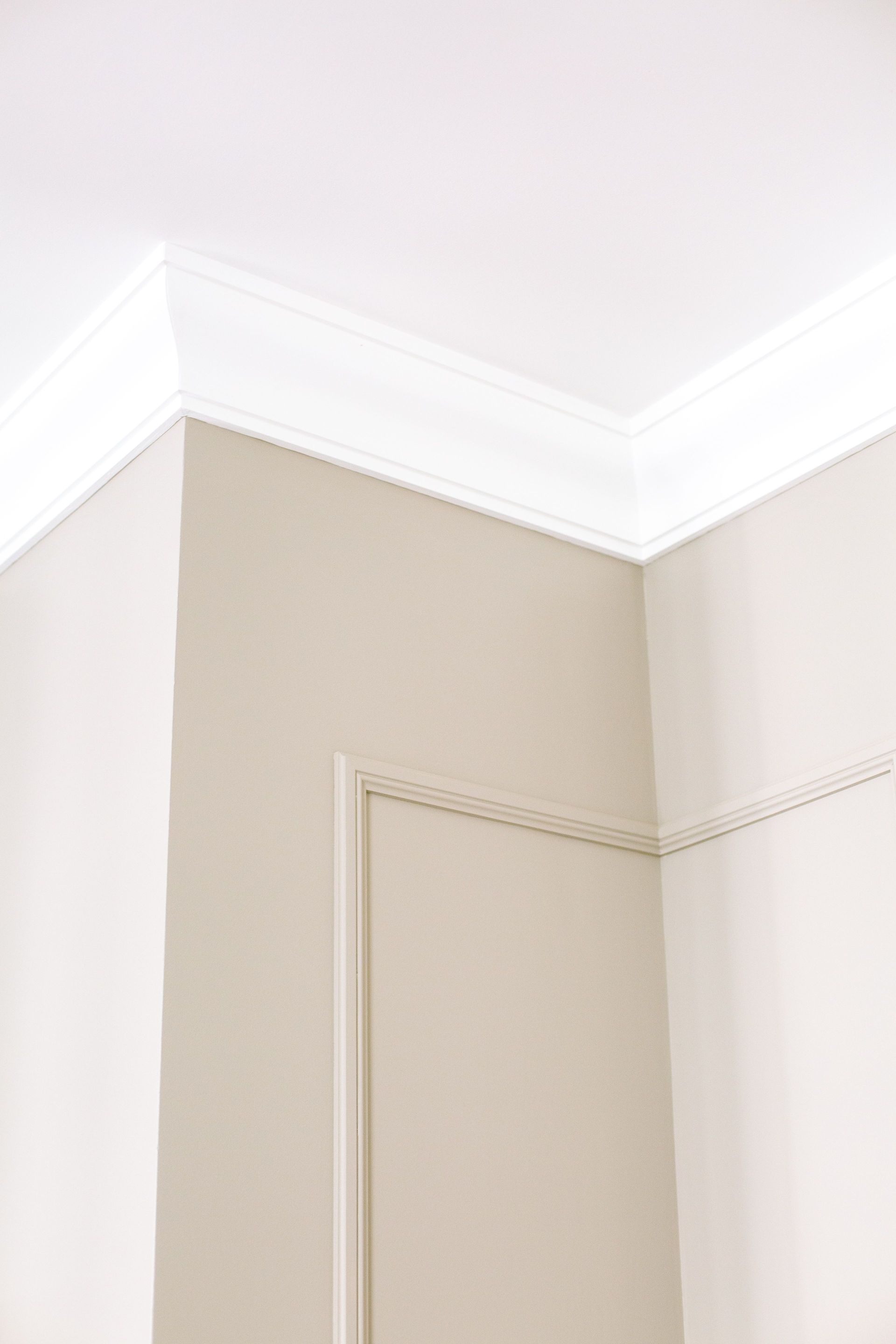 Close-up of intricate ceiling moulding and beige walls with minimalist design, showcasing home renovation details.